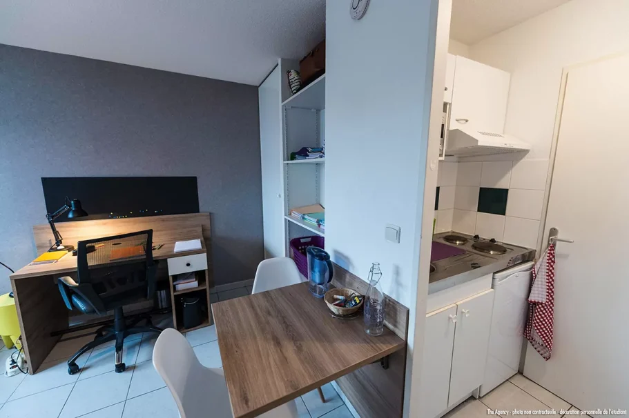cuisine salon Petit appartement avec bureau, cuisine et table pour deux. Mur gris.