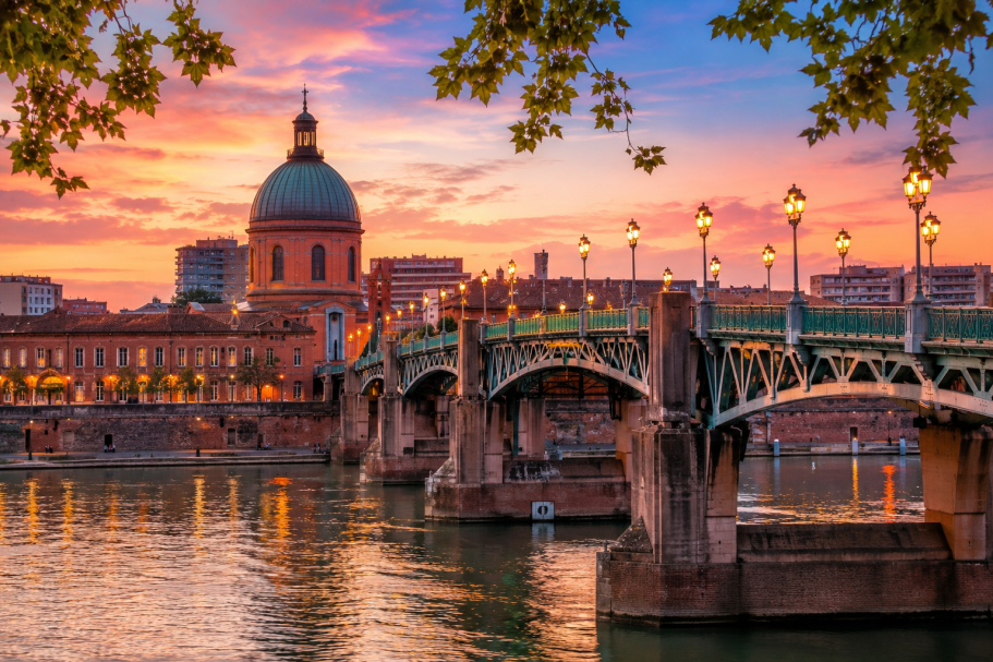 Pont sur la rivière au crépuscule, avec une cathédrale et des lampadaires éclairés.
