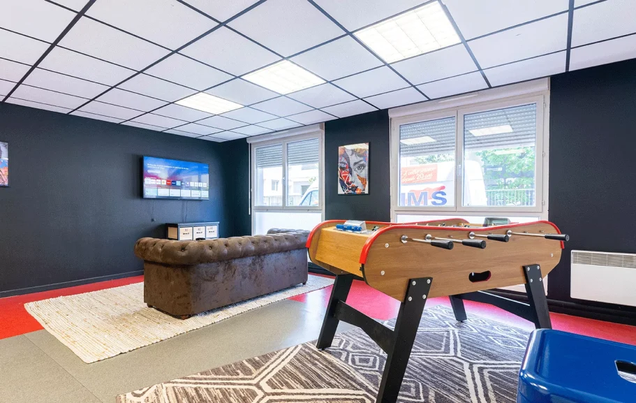 Salle de jeux moderne avec un baby-foot, canapé et télévision. Murs noirs, sol clair.